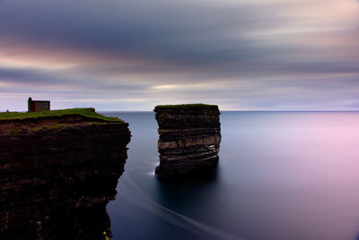 Rock formation by sea against sky during sunset