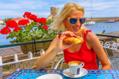 Smiling woman wearing sunglasses eating food sitting at cafe