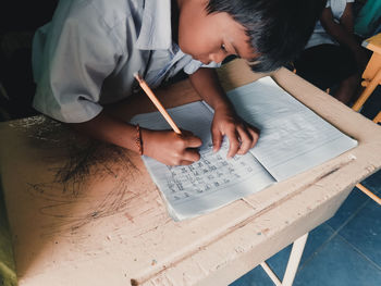 High angle view of boy writing on book in classroom