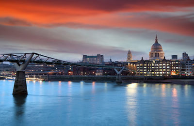 Illuminated bridge over river against cloudy sky