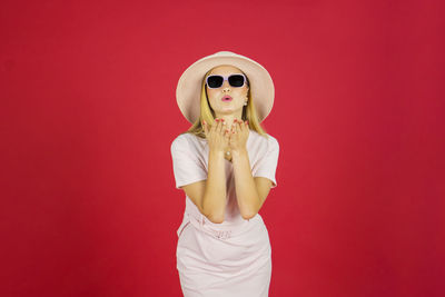 Young woman wearing sunglasses standing against red background