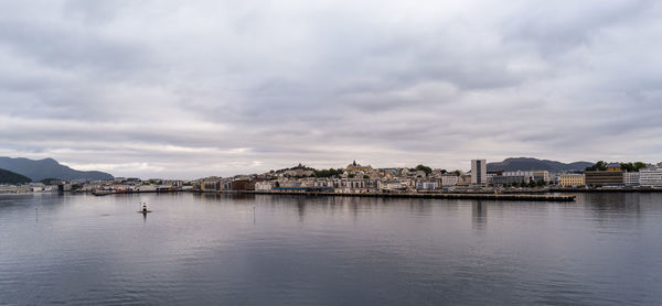 View of buildings by river against cloudy sky