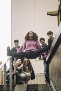 Low angle view of girl doing splits with male and female friends near staircase