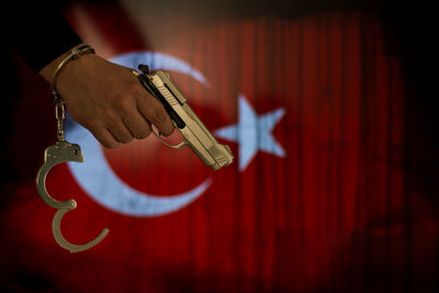 Cropped hand of male criminal holding gun against turkish flag