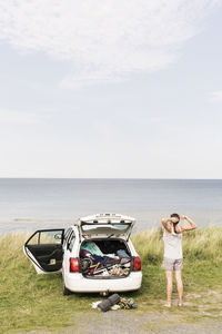 Rear view of woman stretching by car on field against sea