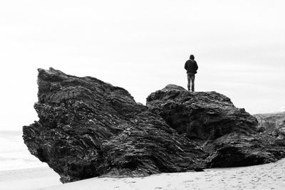 Rear view of man standing on rock at beach against sky