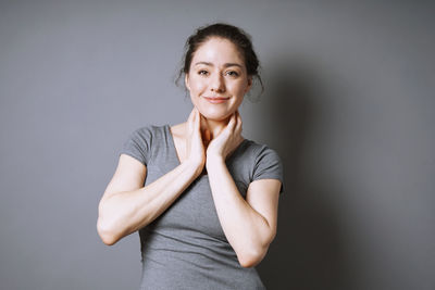 Portrait of young woman standing against gray background