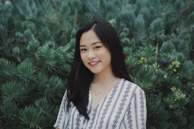 Portrait of smiling young woman standing against plants