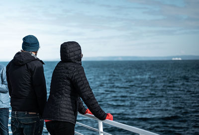 Rear view of people standing by railing of nautical vessel on sea against sky