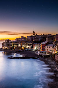 Illuminated cityscape by sea against clear sky at night