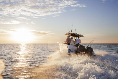 Men enjoying in speedboat at sea against sky during sunset