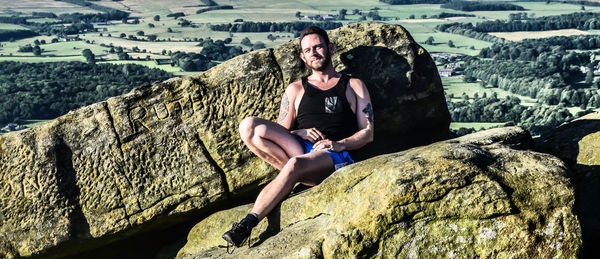 Portrait of man sitting on rock against sky