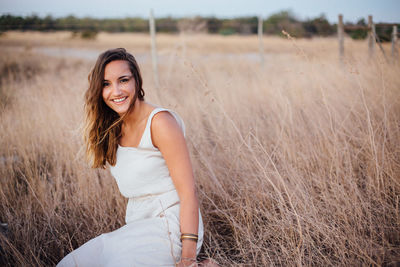 Portrait of smiling young woman sitting on dry grass