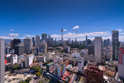 Aerial view of buildings in city against blue sky