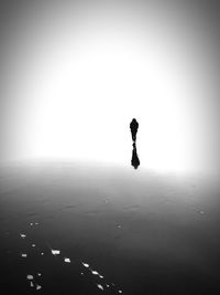 Silhouette man walking on beach against clear sky