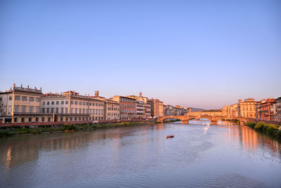 Buildings by river against clear blue sky