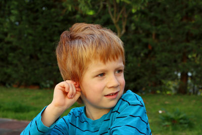 The blond boy looks into the distance with interest, pinching his ear.a boy looks away with a smile.