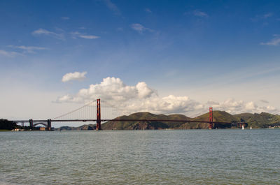 View of suspension bridge over river against cloudy sky