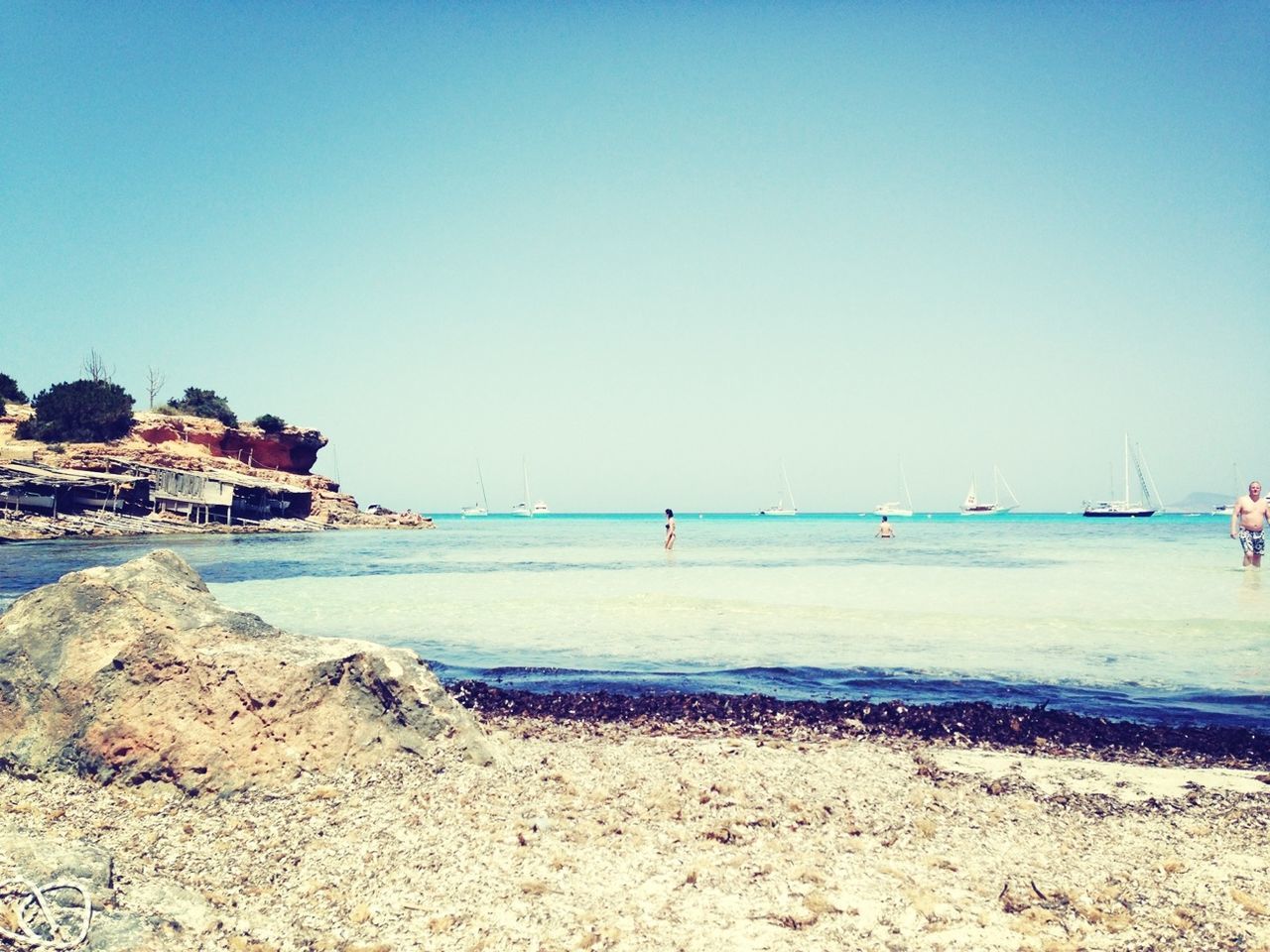 clear sky, water, sea, copy space, beach, blue, shore, tranquility, tranquil scene, sand, scenics, rock - object, nature, beauty in nature, built structure, horizon over water, coastline, incidental people, architecture, day