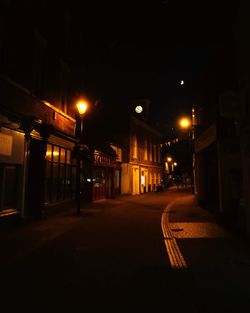 Empty road amidst illuminated buildings at night