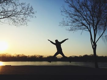 Silhouette man jumping by lake against clear sky