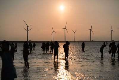 Silhouette people on shore against sky during sunset