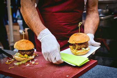 Midsection of man preparing burger at table in kitchen