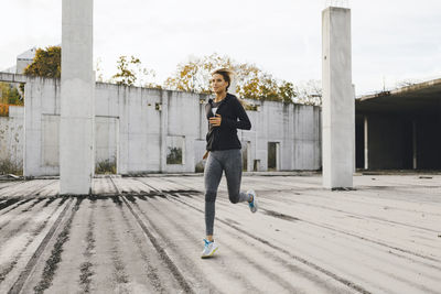 Full length of young woman running on footpath