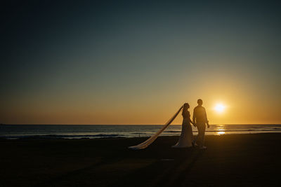 Silhouette people on beach against sky during sunset