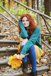 Portrait of young redhead woman sitting on autumn leaves