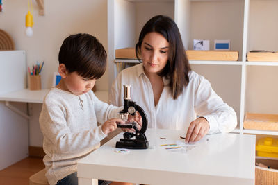 Mother assisting son in puzzle sitting at home