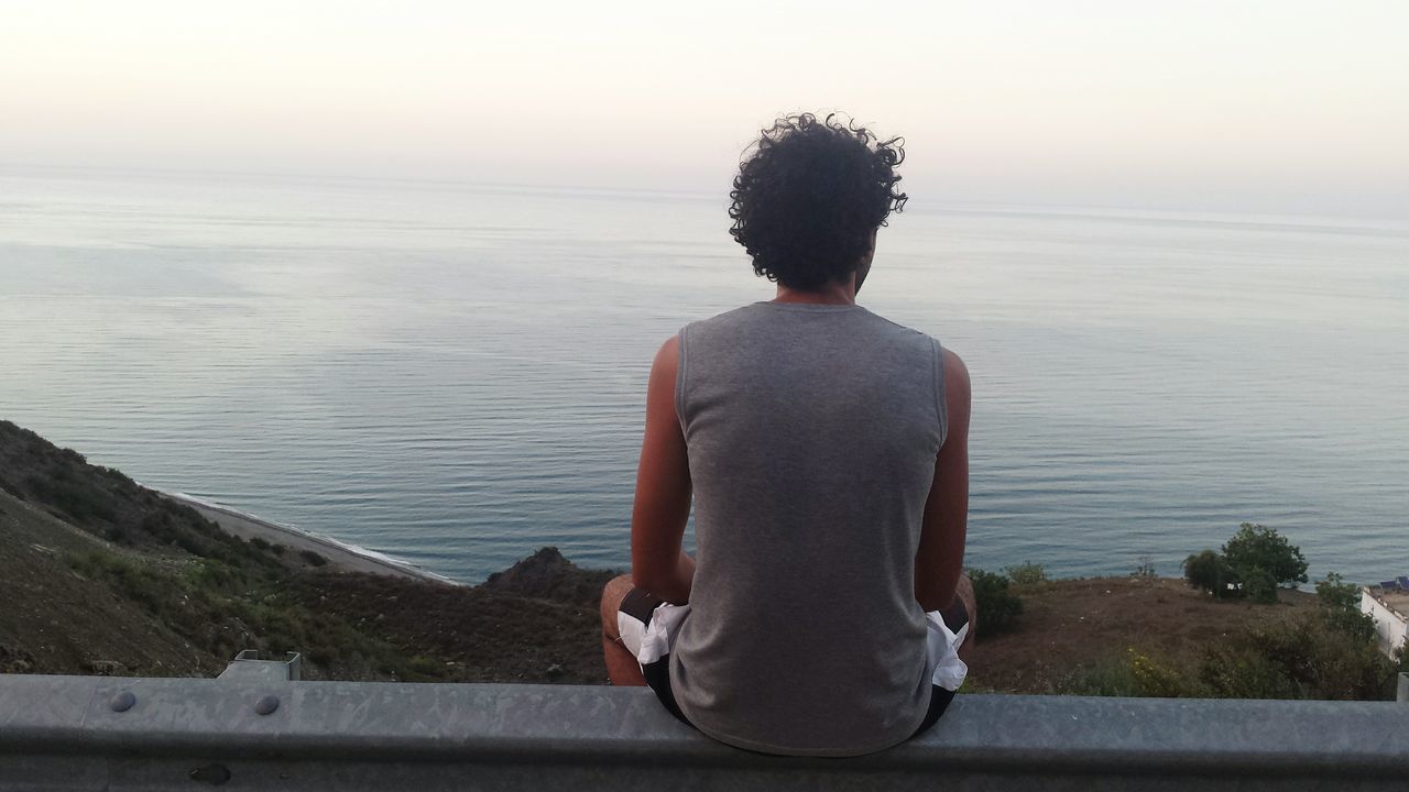 REAR VIEW OF MAN SITTING ON ROCK