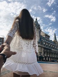 Rear view of woman holding hand of man outside building