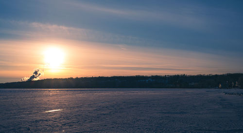 Scenic view of frozen field against sky during sunset