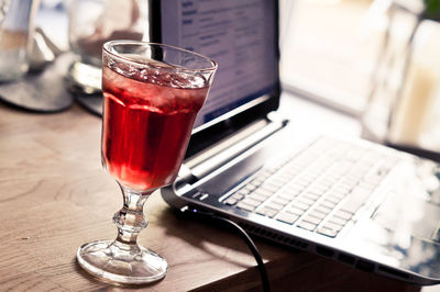 Close-up of red drink in glass by laptop on table 