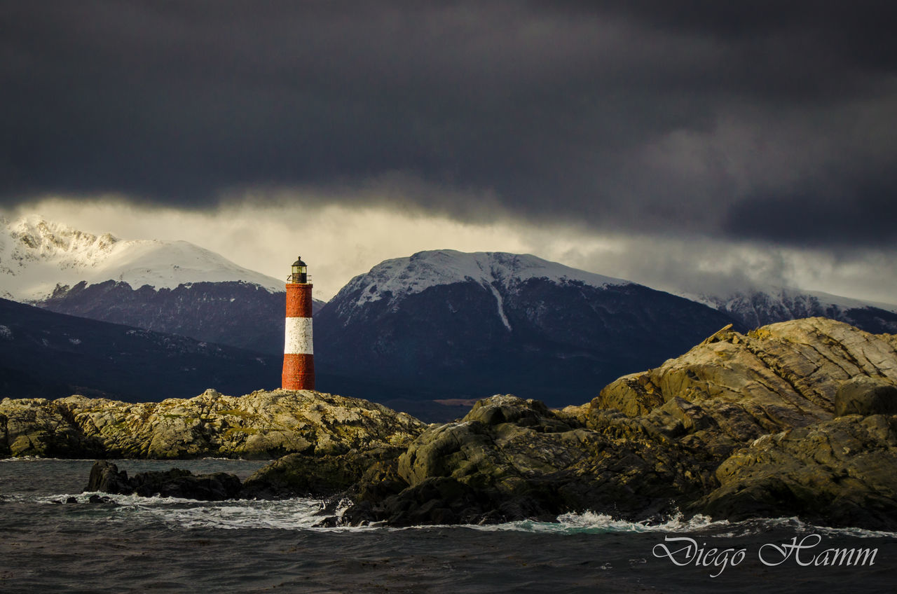 LIGHTHOUSE BY ROCKS AGAINST MOUNTAIN RANGE