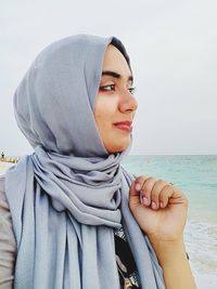 Smiling young woman wearing hijab looking at sea