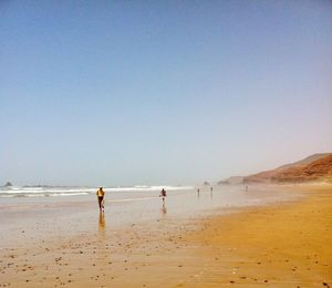 Men standing on beach against clear sky