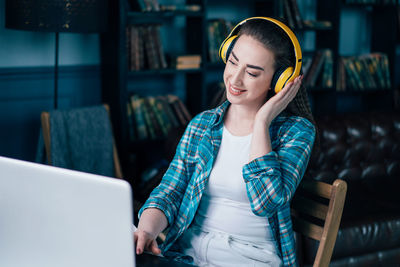 Young woman listening music while using laptop