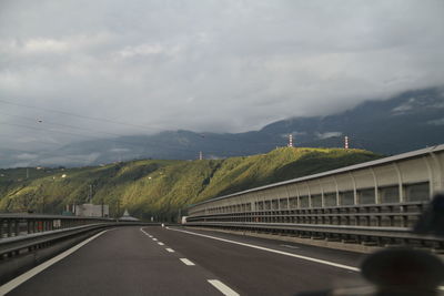 Road leading towards mountains against cloudy sky