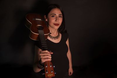 Portrait of woman holding guitar against black background