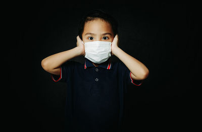 Portrait of boy standing against black background