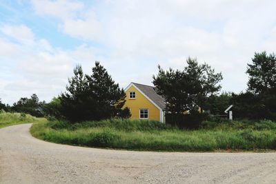 Road amidst trees and buildings against sky