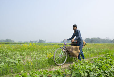 Young farmer riding bicycle on field carrying vegetable bag