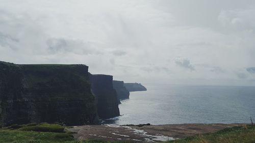 Scenic view of sea by cliff against sky