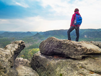 Woman cary blue back pack wear red jacket watch over landscape from mountain summit.