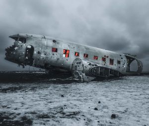 Abandoned airplane on frozen land against cloudy sky