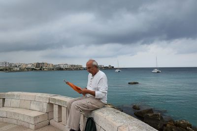 Woman sitting by sea against sky