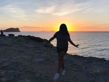 Rear view of woman standing on beach during sunset