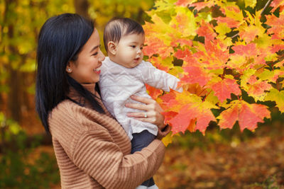 Mother and daughter in park touching autumn leaf at park